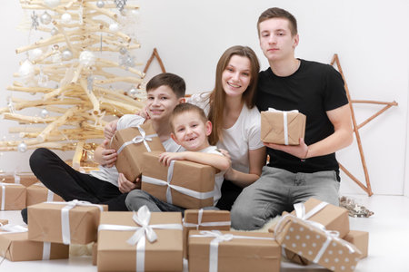 Holidays Concept. cute teenagers are sitting by the wooden decorations Christmas tree and many gift...