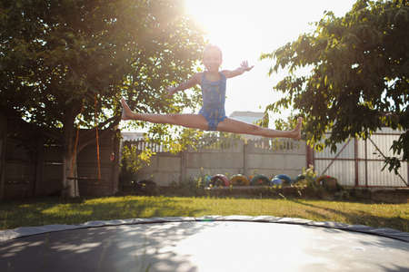 little sports girl jumps on a trampoline. Outdoor shot of girl jumping on trampoline, enjoys jumping in home. happy summer vacation.の写真素材