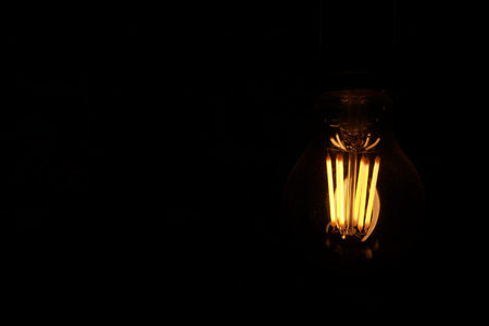 Classic Edison light bulb on black background with space for text.