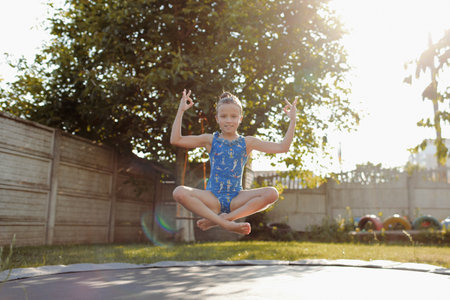 little sports girl jumping on a trampoline. Outdoor shot of girl jumping on trampoline, enjoys jumping in home. happy summer holiday.の写真素材