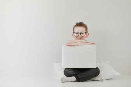 schoolboy in glasses using laptop sitting on bed. Child doing school homework and seriously and...