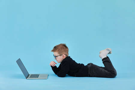 distance learning online education. Schoolboy studying at home with laptop and doing school homework on blue background.の写真素材