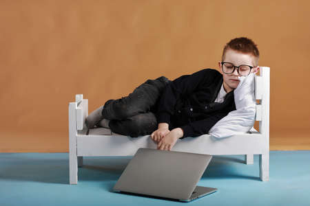 Portrait of casually dressed little boy leaning on white pillow, while hugging it, feeling tired after long full day, with cheerful smile, having rest.の写真素材