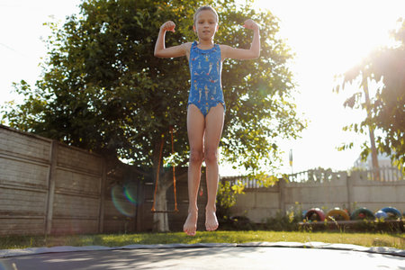little sports girl jumping on a trampoline. Outdoor shot of girl jumping on trampoline, enjoys...