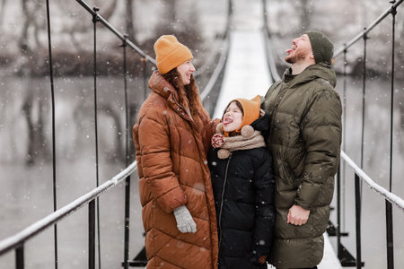 Young mother, father and the little daughter catches snowflakes in a beautiful winter park during a...