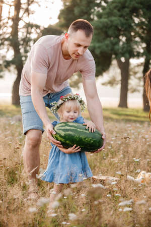 young father And Little Daughter Enjoying Family Picnic holding big Watermelon In Beautiful summer Park. Weekend With Father Concept.の写真素材