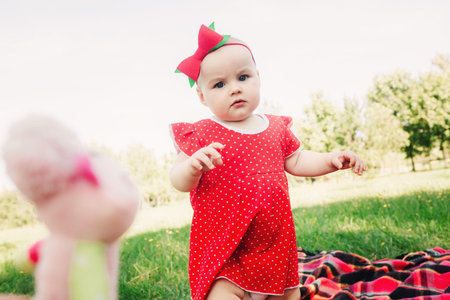 Cute 10 months baby girl on picnic on grass with watermelons. child in red dress and bow on head. Concept of healthy eating, childhood, fruit ripeness, parenting, seasonal harvestの写真素材