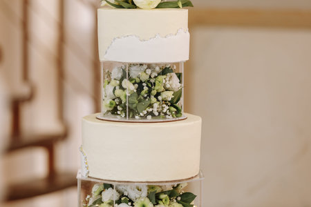 wedding cake. Close-up photo of a beautiful white three-tiered wedding cake decorated by flowers and greenery.の写真素材