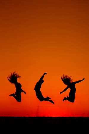 silhouette of three people jumped into the sunrise.の写真素材