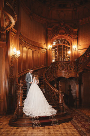 wedding day. beautiful bride in white long dress and young groom wearing in black suit are hugging...