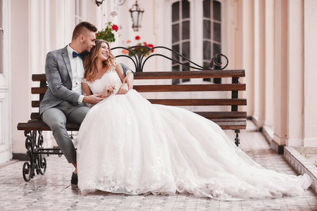 wedding day. beautiful bride in white long dress and young groom wearing in black suit are hugging in historic europe town.の写真素材