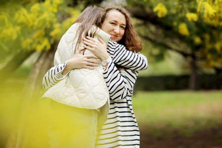 young mother and daughter are holding a mimosa branch and sitting on the tree in the blooming park. Mom and child spending time together, having fun at the mimosa orchard. Mother's, baby's day.の写真素材