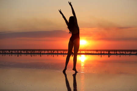 silhouette of a young slim woman in a swimsuit dancing at sunset on the sea. summer holiday.の写真素材