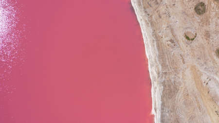 Flying over a pink salt lake. Salt production facilities saline evaporation pond fields in the salty lake. Dunaliella salina impart a red, pink water in mineral lake with dry crystallized salty coastの写真素材