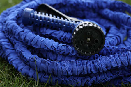 close up of watering hose lies on the grassy ground. blue rubber tube with device for spraying and watering plants in the garden. selective focusの写真素材