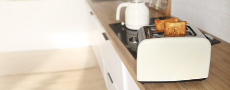 banner of Modern white toaster and roasted bread slices toasts inside on wooden table in kitchen....