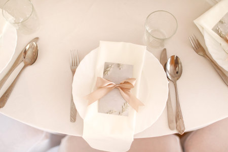 Wedding table setting with white plate, glasses and silver cutlery. mockup blank with pink ribbon on...