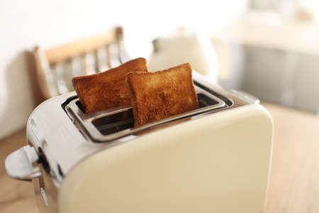 Toasted bread and toaster for breakfast. Modern white toaster and roasted bread slices toasts inside on wooden table in kitchenの写真素材