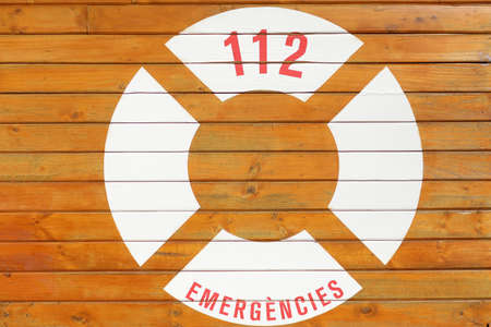 Emergency post in the Castellon tourist resort of El Grau. Signs orange lifebuoy in the foreground and 112 on wooden board. High quality photo.の写真素材