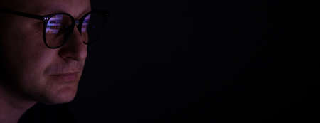 male working online late. Close up side view of focused man wears computer glasses for reducing eye strain blurred vision looking at pc screen with computer reflection using internet, watching.の写真素材