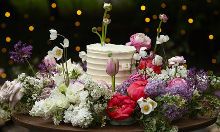 white wedding cake with fresh roses and wild flowers outdoors. Wedding decoration table in the...