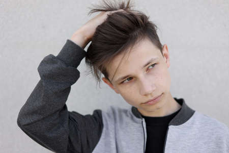 Handsome young man with stylish haircut. Portrait of teen boy with youth hairstyle is standing on gray backgroundの写真素材