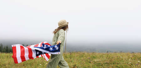 Beautiful child girl in hat with the American flag on foggy mountains. Independence Day of United States USA on 4th of July with family. freedom. American patriotic holiday concept.の写真素材
