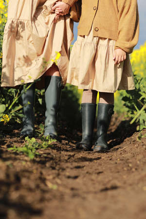 mother's day. cropped photo of moms and child daughters legs in rubber boots is walking in the rapeseed field. Family having fun on the nature. Concept of friendly family vacationの写真素材
