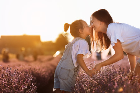 mother's day. young beautiful mom and adorable child daughter enjoy walking hand in hand in a lavender field at sunset light. Maternal care and love for the child. family day. family look.の写真素材