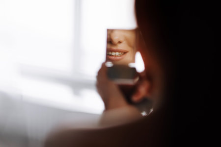 smiling beautiful young woman looks in the mirror with love of lipstick on it. girl with make up and...