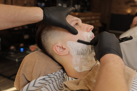Barber Man is shaving client with a vintage straight razor in a barbershop. Shaving cream, foam....