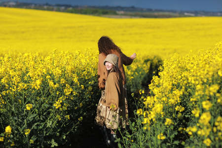 young mother and child daughter playing in the yellow rape fields. Family is having fun on the nature. Concept of friendly family and of summer vacation. mothers day and baby day. back view.の写真素材