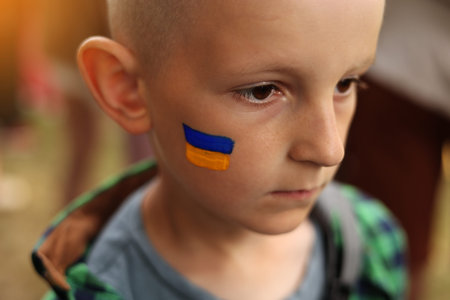 close up of smiling child with painted Ukrainian flag on face. Protest against Russian war invasion...