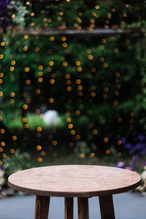 Round wooden table on a green nature with light bulbs background. outdoor table at desk. Grass, greens and party decoration bushes in the backgroundの写真素材