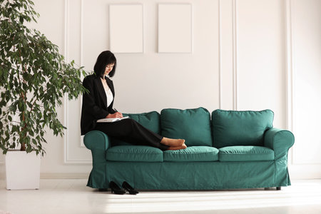 Confident young brunette business woman looking at camera on white wall background.Studio portrait of successful friendly female with short hair in black suit and white blouse with jacket on shoulder.の写真素材