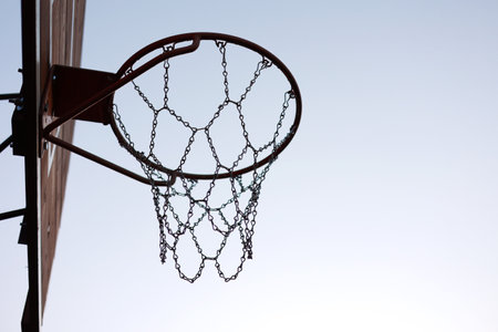 silhouette of basketball hoop with metal net on wooden backboard on sunset sky background. Basketball court outdoors. Recreational sport equipment on streetball field alfresco, playground on streetの写真素材