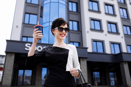 Happy lawyer businesswoman professional is walking outdoors talking on cell smart phone. Caucasian successful female is smiling wearing stylish white-black dress with black bag.の写真素材