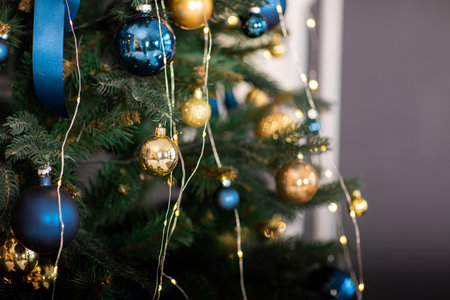 Fir tree decorated with christmas gold and blue balls. Close-up of beautiful christmas tree with illuminated garland and blue ribbons. Merry Xmas and Happy Holidays greeting card, New Year. Noelの写真素材