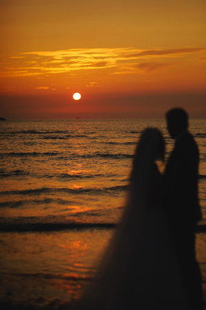 Silhouette of newlyweds bride and groom are hugging on sunset or sunrise on beach. Loving couple by the sea. Ocean romantic ceremony. wedding day. February 14, St. Valentine's Day. honeymoon.の写真素材