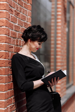 Businesswoman talking on the smartphone, working on a laptop and drinking coffee at cafe on terrace in urban city. Communication with clients remote. Coffee break, business concept. working outdoors.の写真素材