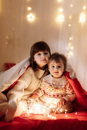 Merry Christmas and Happy Family Holidays. Cheerful cute children girls wearing in Xmas red pajames having fun on white background. Smiling older sister sitting on chair and playing. Loving sibling.の写真素材