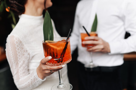 hands of woman and man are clinking, cheers with glasses of Spritz cocktail. Couple celebrating wedding, anniversary with Aperol spritz cocktails, with orange and greens Refreshing alcoholic drink.の写真素材