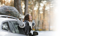 banner Happy woman looks from the car window with a illuminated Christmas tree on a rooftop. Concept of New Year preparation. Idea of fairy tale and festive mood in wintertime. happy winter holidaysの写真素材