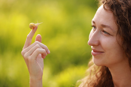 A small snail on the finger on green nature background, snail slime skin care, slime application in cosmetology, cream, tissue regeneration, skin rejuvenation, benefits, edible, farm, French cuisineの写真素材