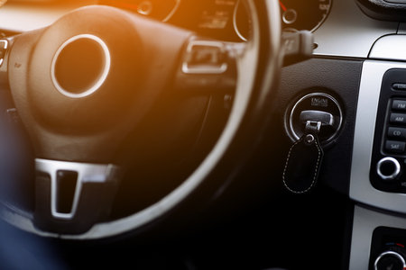 Interior look of steering wheel with airbag and dashboard panel with ignition key of new car. Modern luxury vehicle interior, auto detail. Blurred image of car interior dashboard, lighting.の写真素材