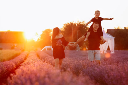 happy family day. Young mother and father carrying on shoulders daughter in lavender field on sunset. Dad, mom and child girl having fun on nature on summer. Concept of friendly family. family look.の写真素材