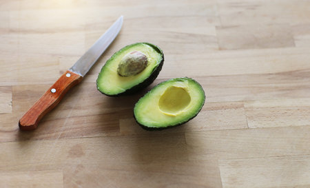 Two slices of fresh organic hass avocado on wooden table background. One slice with core. Raw fruits...