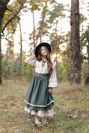 Portrait of little caucasian girl looking at camera standing outdoors. Stylish adorable smiling child in black hat enjoying childhood testimonial concept at green park backgroundの写真素材