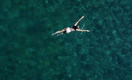 Above view of woman swimming at sea. Aerial top view of young girl in white swimsuit floating on water surface in crystal clear turquoise sea. Vacation at Paradise. Ocean relax, travel and vacation.の写真素材