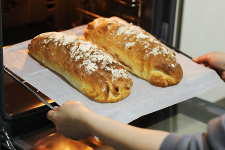 Cropped photo of womans hands take out hot fresh baked breads from an electric oven on metal tray in...